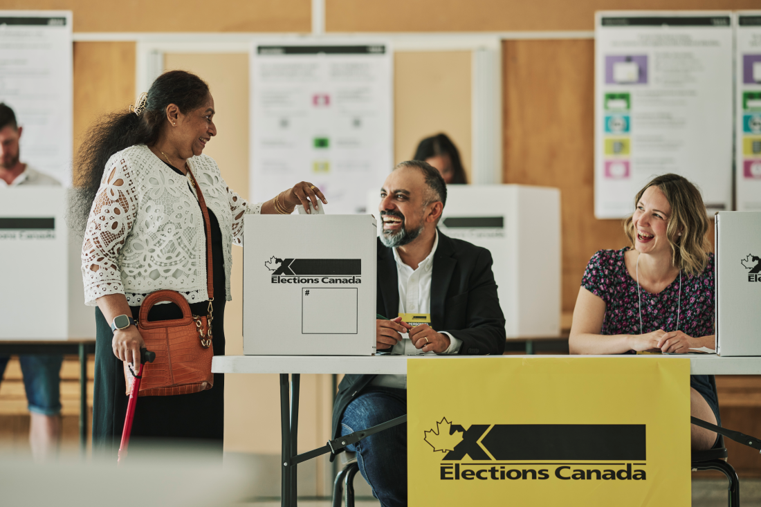 Woman votes at elections canada polling station with two staff looking on and smiling