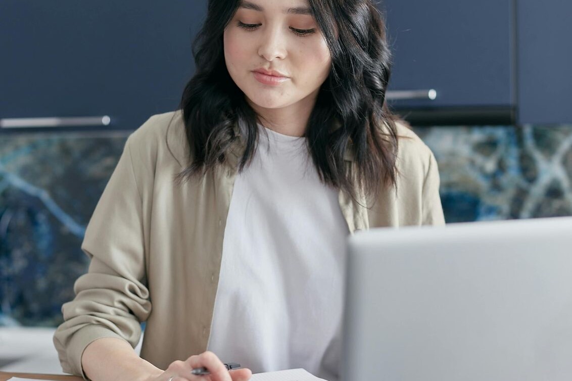 woman types on calculator with papers and laptop open in front of her