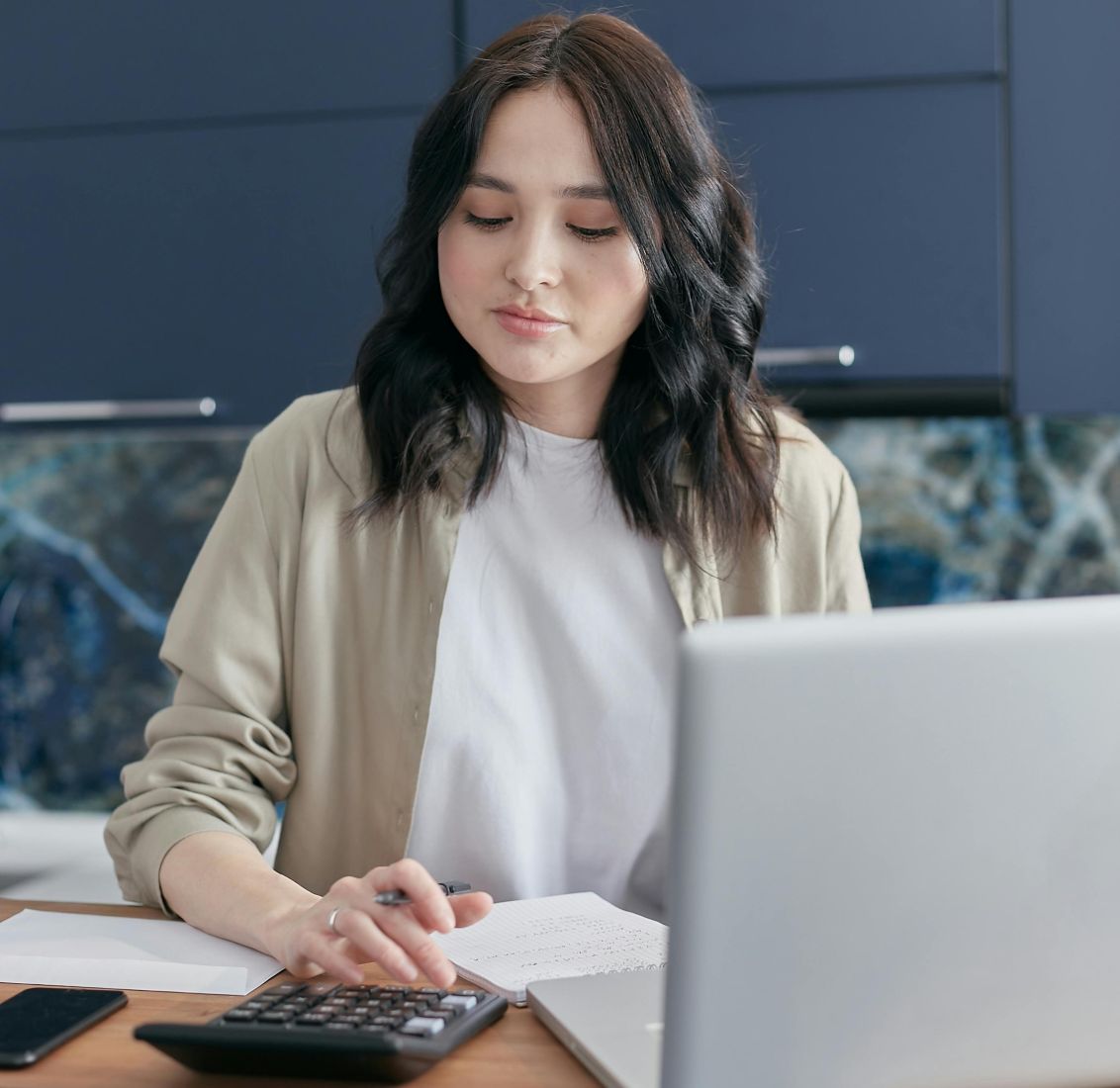 woman types on calculator with papers and laptop open in front of her