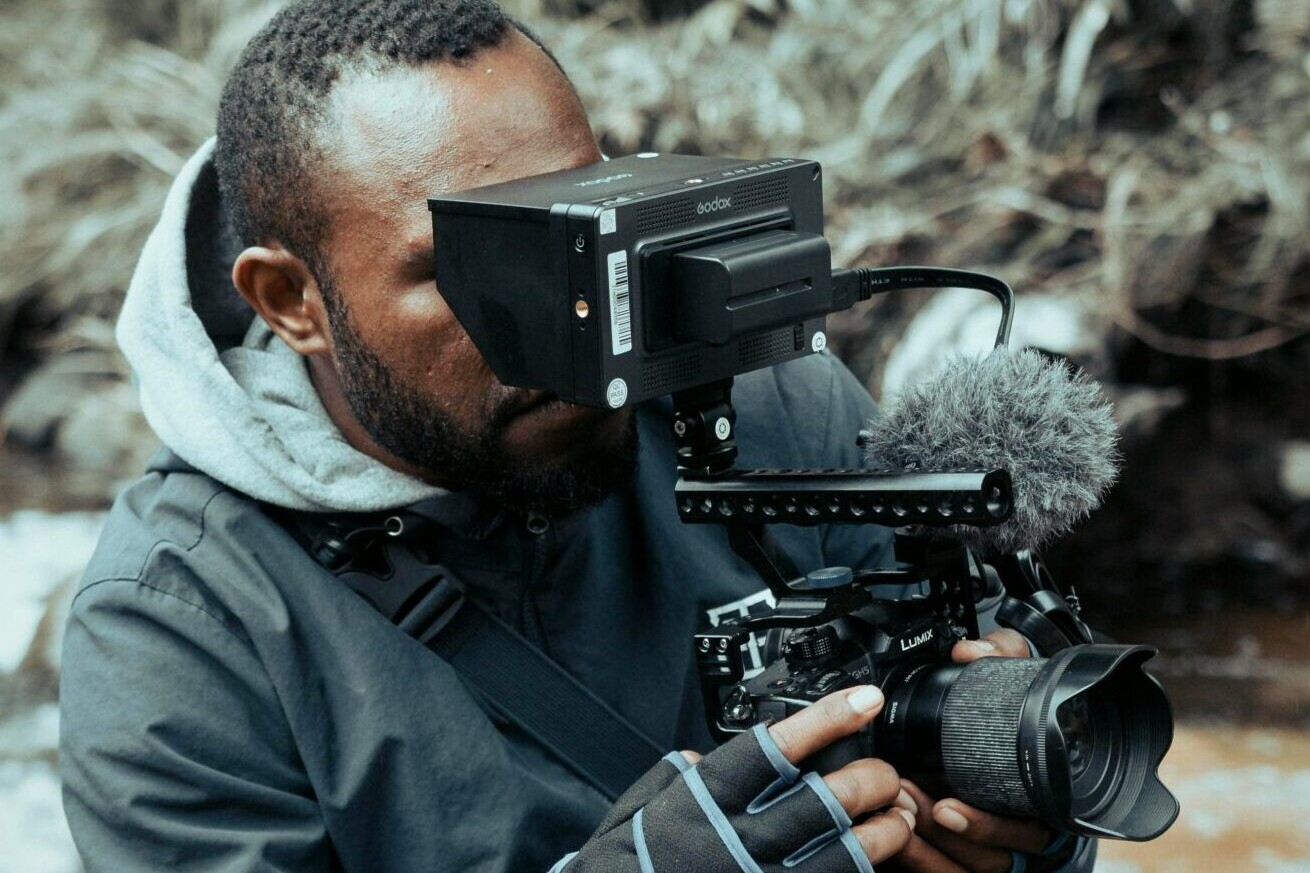 Man behind a film camera shooting outside near a river