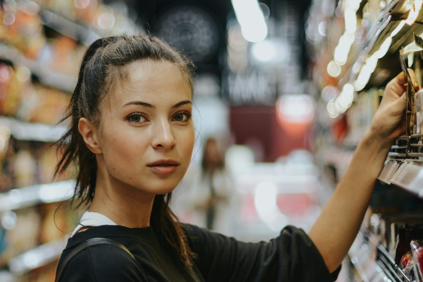 woman in grocery store aisle reaching for product on shelf