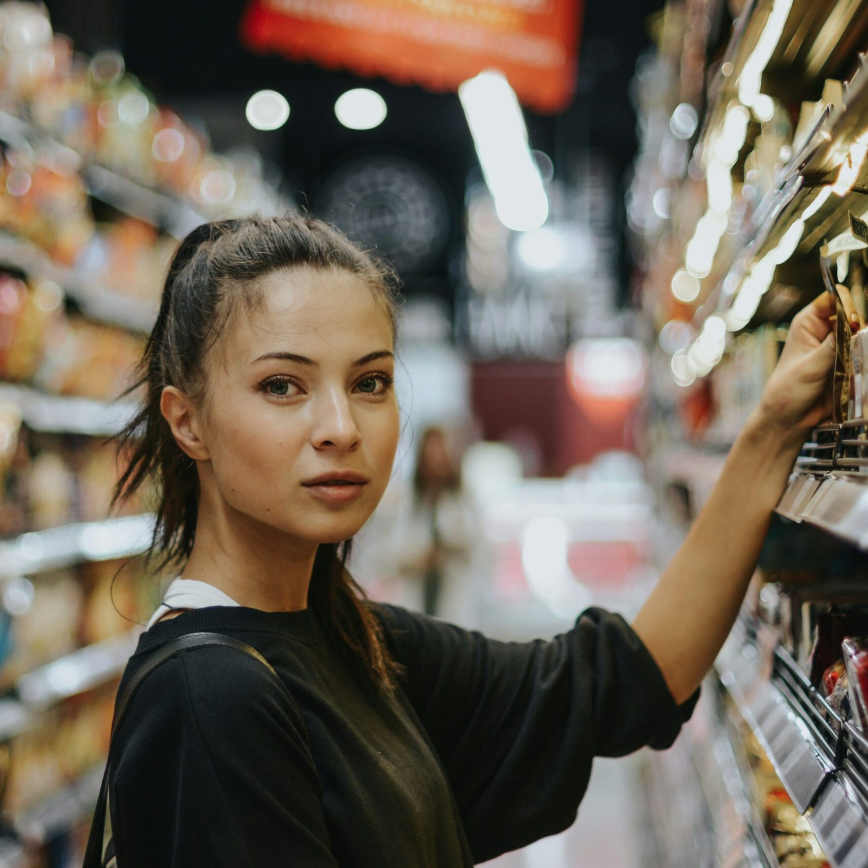 woman in grocery store aisle reaching for product on shelf