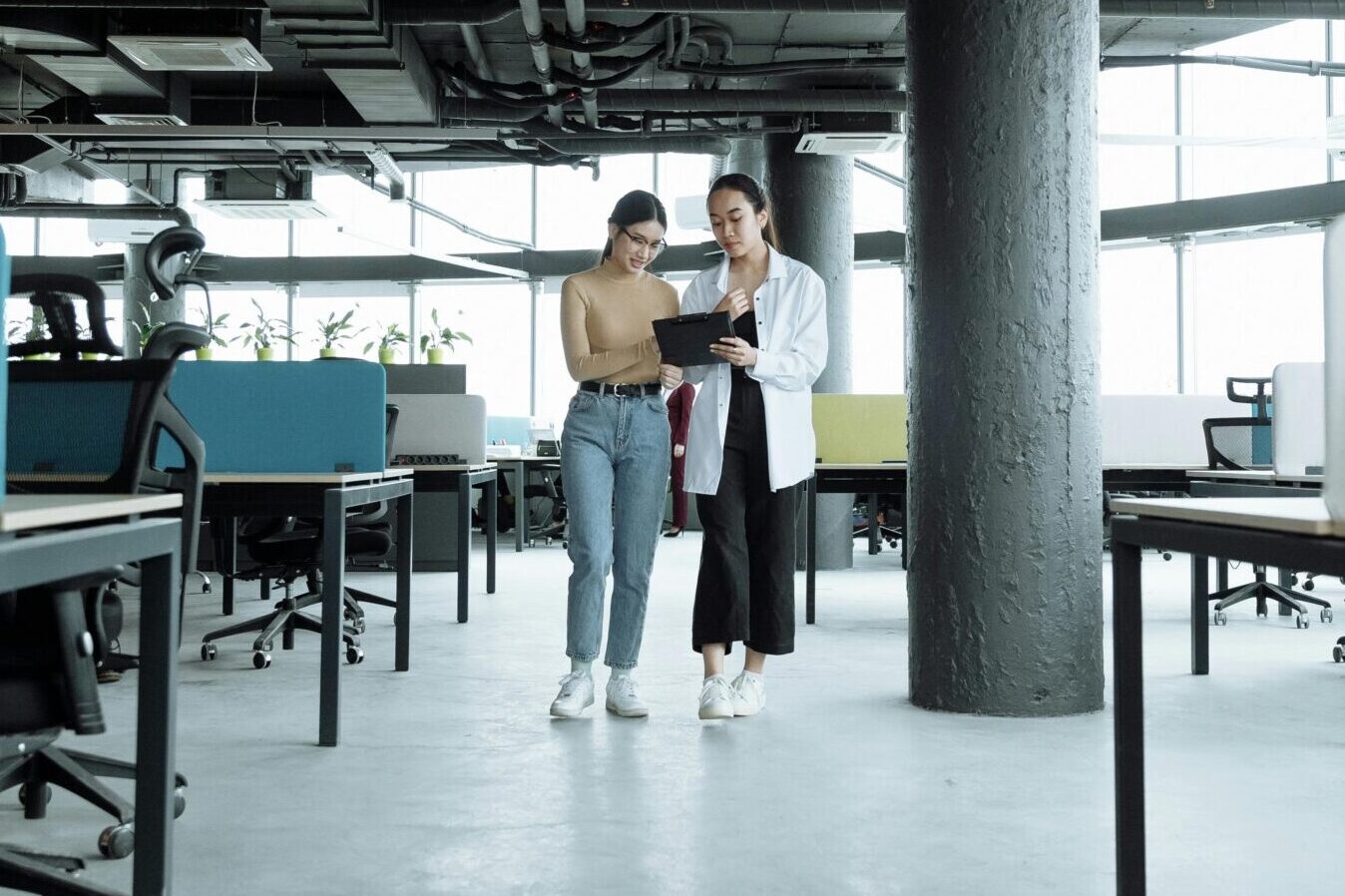 Two women walk in tech office looking at iPad