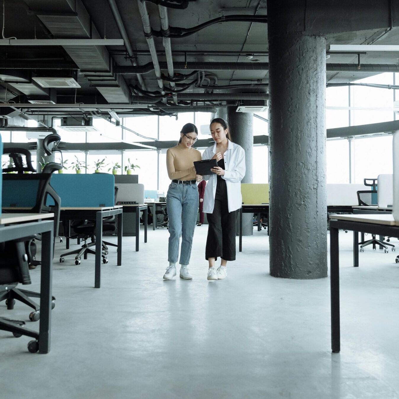 Two women walk in tech office looking at iPad